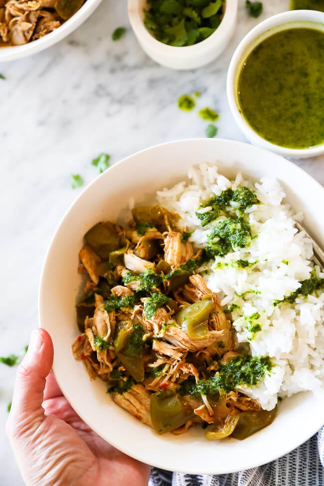 Holding a bowl of easy harissa chicken with rice and a green sauce drizzled on top. 