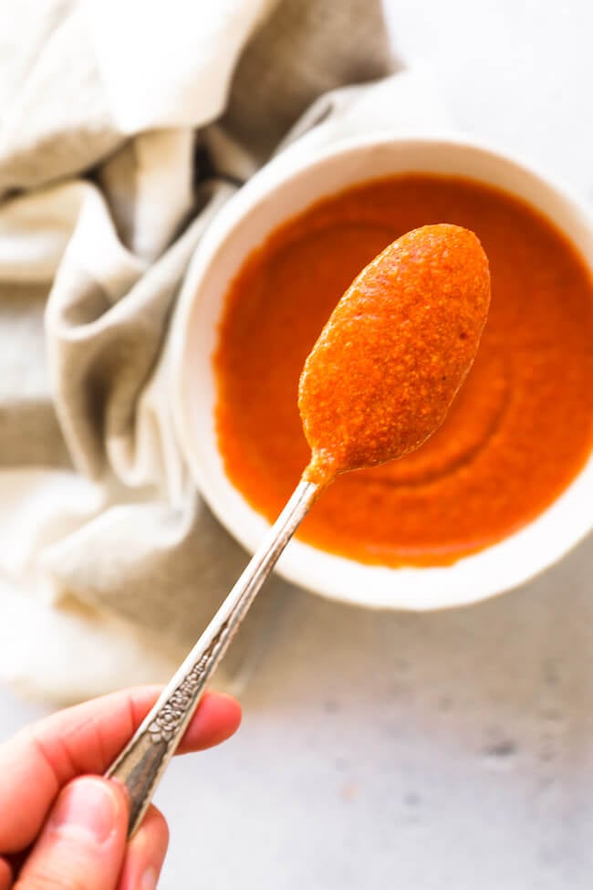 Spoon full of buffalo sauce being held up to the camera with a ramekin full of sauce in the background