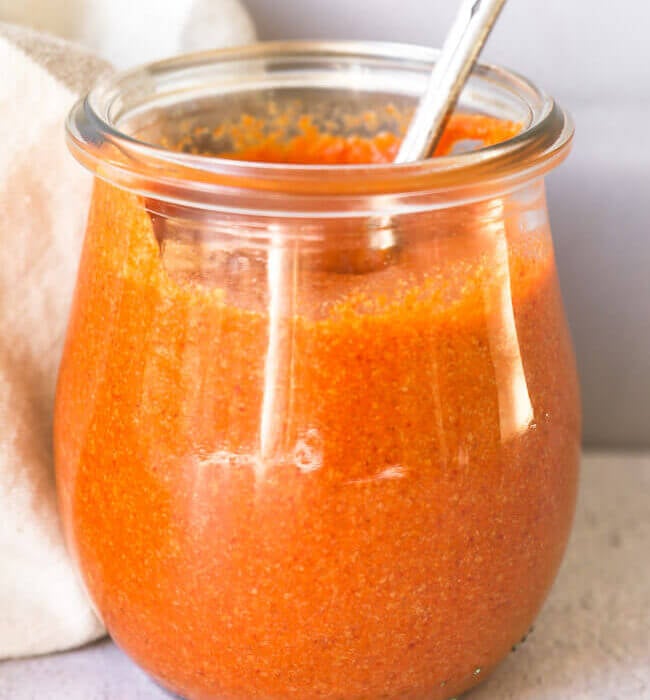 Homemade keto buffalo sauce in a small jar with spoon coming out