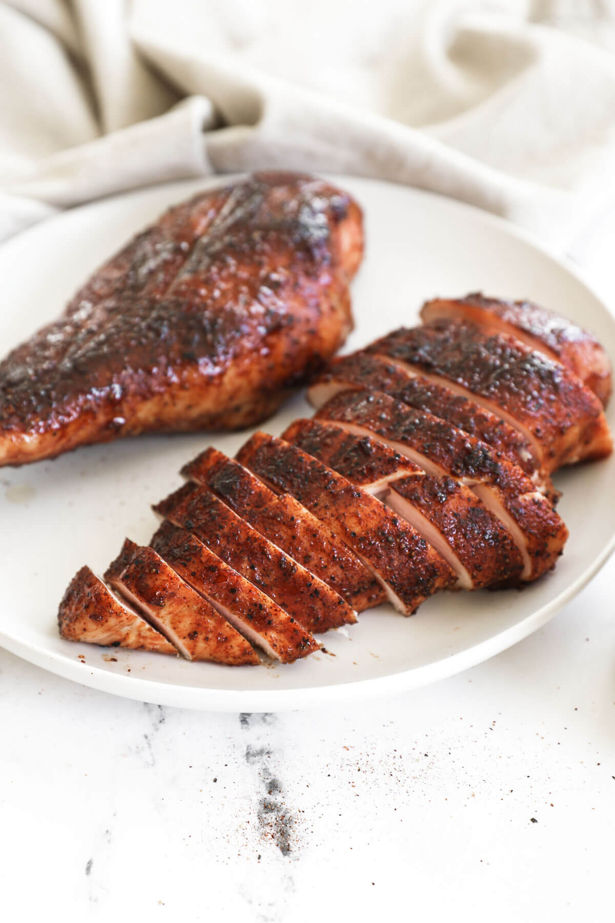 Angled image of two pieces of chicken breast on a plate. The closest image is sliced into strips.