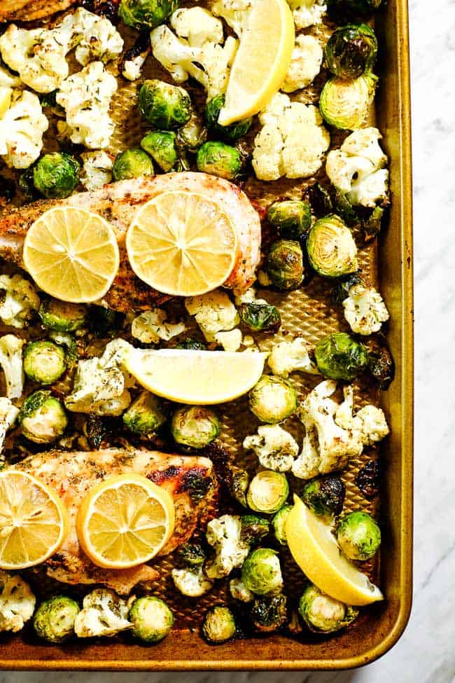 Easy lemon chicken and roasted brussels and cauliflower on sheet pan with lemon slices. 