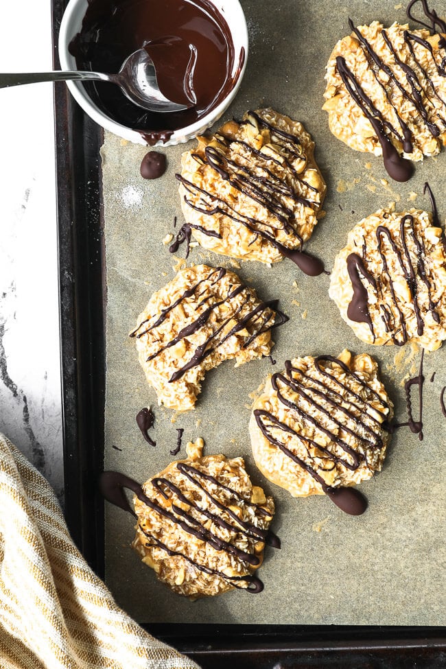 No bake cbd cookies on a cookie sheet drizzled with chocolate on top. One cookie with a bite taken out of it.