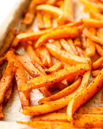 Vertical angled close up image of oven baked butternut squash fries on baking sheet.