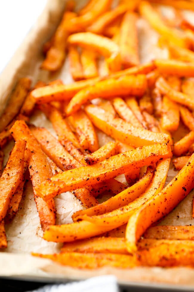 Vertical angled close up image of oven baked butternut squash fries on baking sheet.