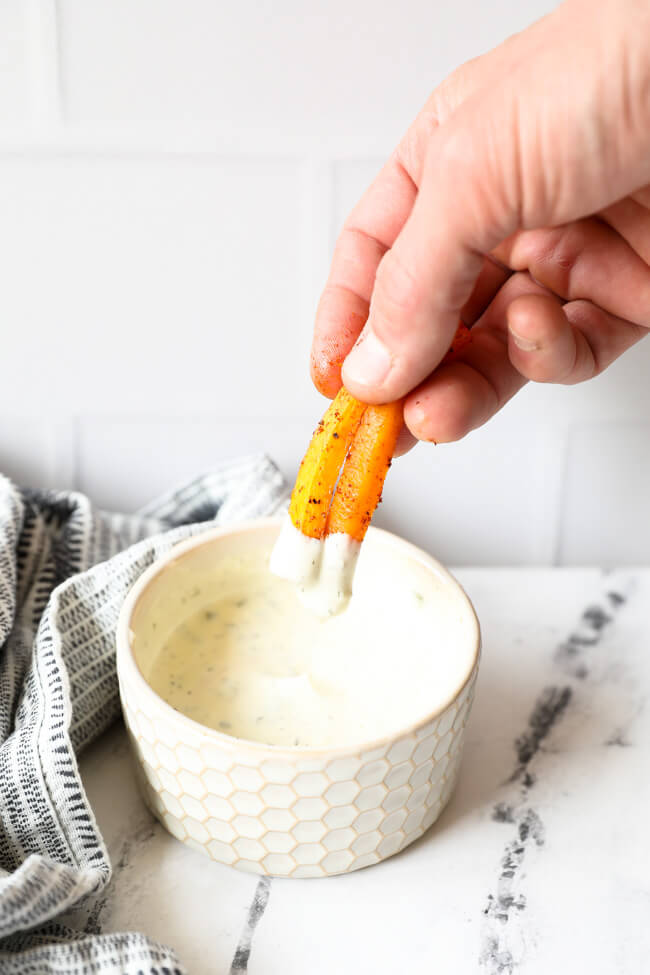 Vertical angled image of dipping two butternut squash fries into ranch sauce.