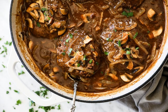 Easy salisbury steak in pan with mushroom and onion gravy. Spoon lifting steak out horizontal image