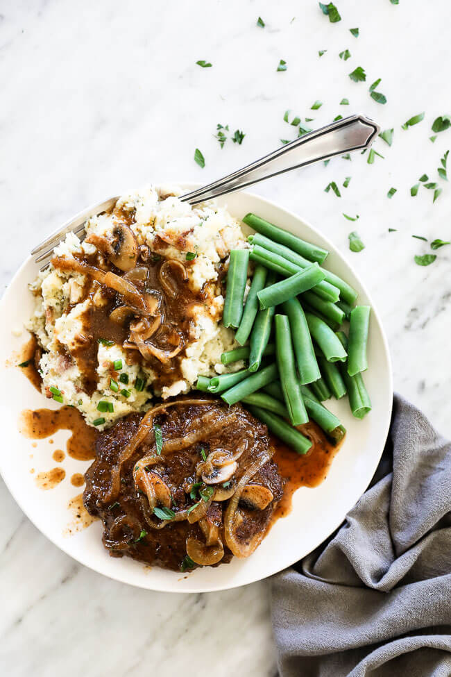 Vertical overhead image of loaded mashed cauliflower served on a plate with salisbury steak and green beans. 