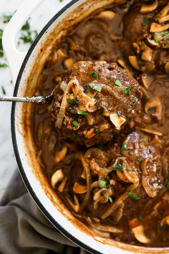 Easy salisbury steak in pan with mushroom and onion gravy. Spoon lifting steak out vertical image