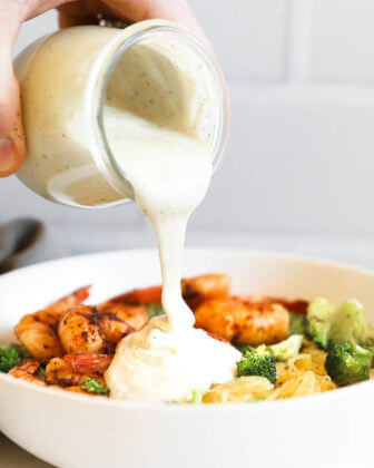 Pouring dairy free alfredo sauce over a bowl of spaghetti squash, shrimp and broccoli to make spaghetti squash alfredo.