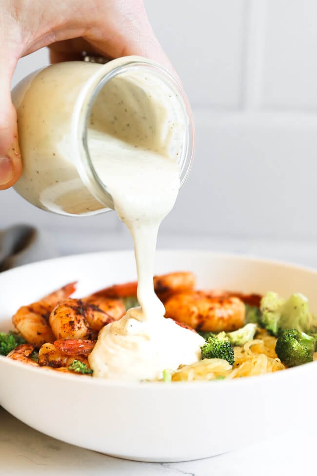 Image of pouring dairy free alfredo sauce into a bowl full of spaghetti squash, shrimp and broccoli to make spaghetti squash alfredo. 