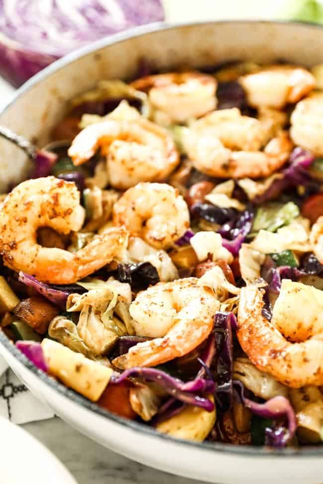 Angled image of skillet with sausage and shrimp, cabbage, zucchini and mushrooms. 