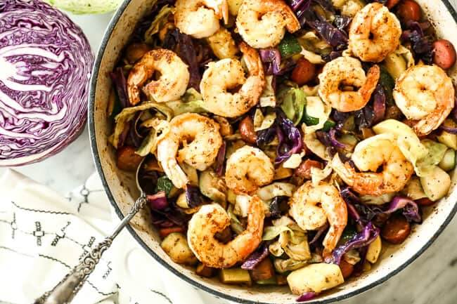 Shrimp and sausage skillet with cabbage, zucchini and mushrooms in a skillet with a serving spoon. 