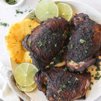 Easy slow cooker jerk chicken on a plate with pineapple and lime vertical image