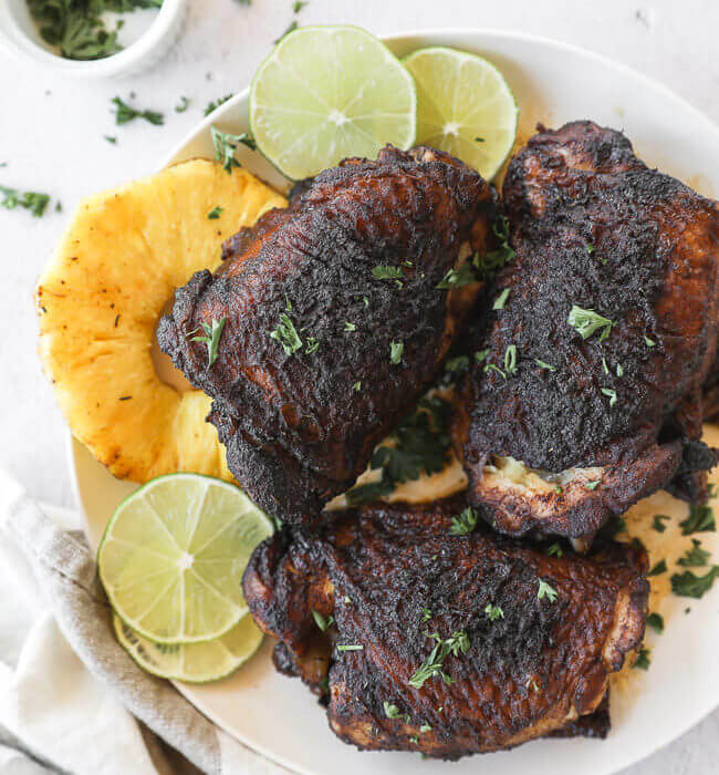 Easy slow cooker jerk chicken on a plate with pineapple and lime vertical image