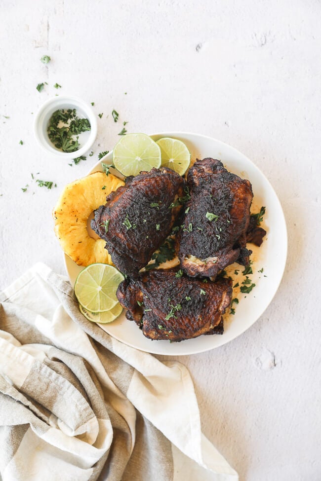 Easy slow cooker jerk chicken on a plate with pineapple and lime vertical pulled out image