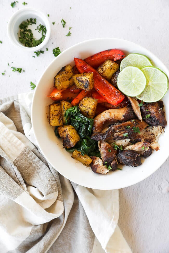 Jerk chicken shredded in a bowl with pineapple, greens, bell pepper and lime with cilantro topping.