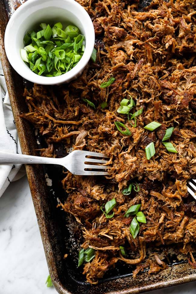 Easy slow cooker pulled pork on sheet pan with two forks and sliced green onions vertical image