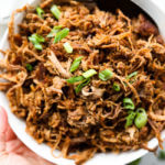 bowl of shredded slow cooker pulled pork with chopped green onions on top