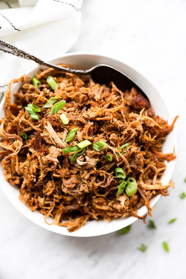 Easy slow cooker pulled pork in a bowl with sliced green onions on top vertical overhead image