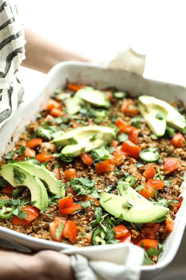 Image of holding easy taco casserole in white casserole dish, topped with chopped tomato, fresh cilantro, sliced jalapeño and avocado. 