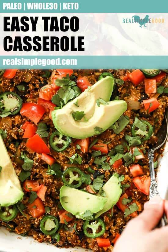 Image of easy taco casserole in white casserole dish with serving spoon, topped with chopped tomato, fresh cilantro, sliced jalapeño and avocado. 