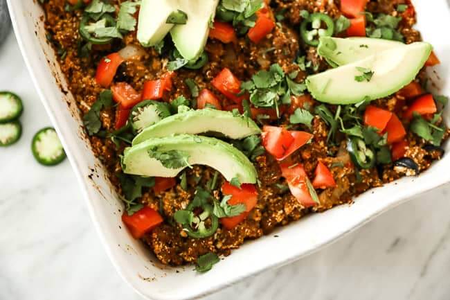 Image of easy taco casserole in white casserole dish, topped with chopped tomato, fresh cilantro, sliced jalapeño and avocado. 