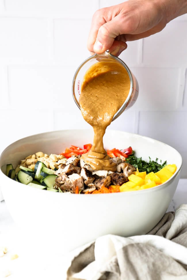 Vertical straight on image of pouring the "peanut" sauce over the Thai chicken salad in a bowl. 