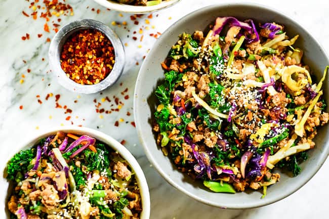 Egg roll in a bowl with sesame seeds on top with cruciferous veggies, ground pork and a savory sauce. 
