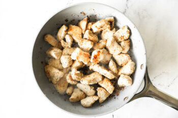Cooked chicken pieces coated with flour in a pan