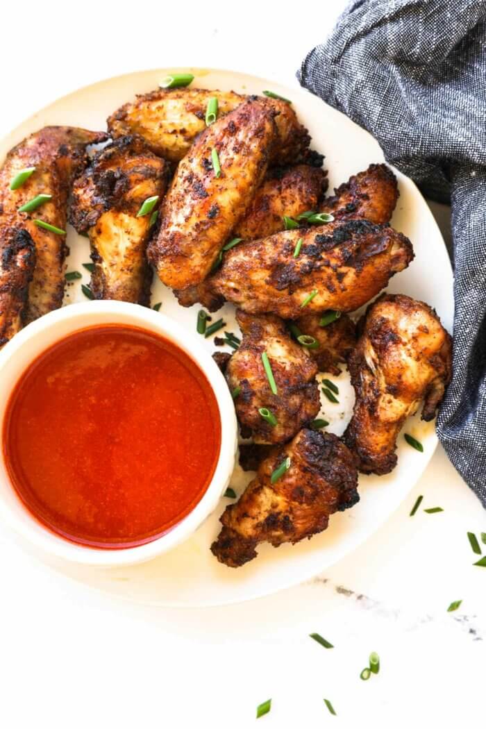 Overhead image of a plate with crispy chicken wings and a ramekin of buffalo sauce.