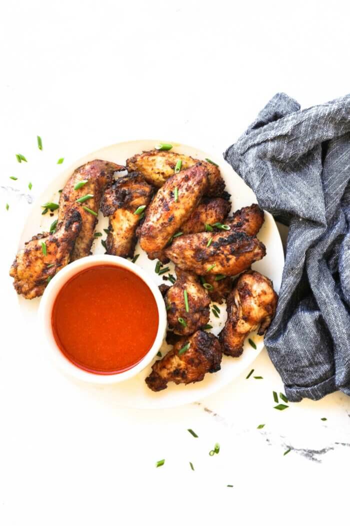 Overhead image of a plate of crispy chicken wings with a side of buffalo sauce. Pulled out to be able to see the full plate. 