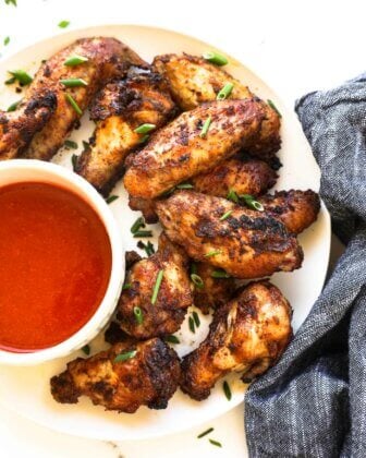 Close up overhead image of crispy wings on a plate with a side of buffalo sauce.