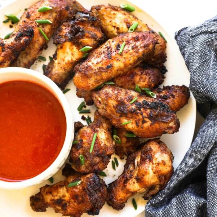 Close up overhead image of crispy wings on a plate with a side of buffalo sauce.