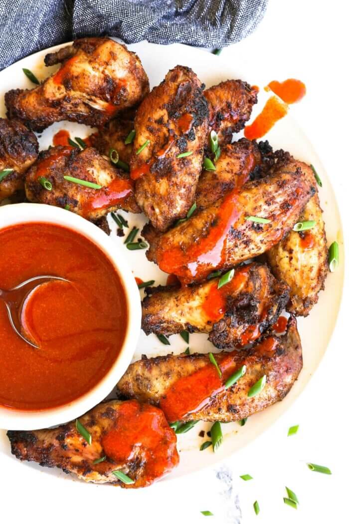 Close up overhead image of chicken wings on a plate with buffalo sauce drizzled on top.