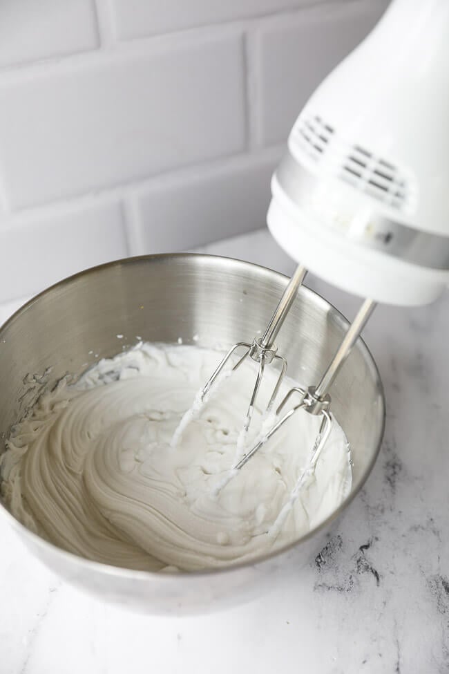 Whipping up coconut whipped cream in a metal bowl with a hand mixer. 