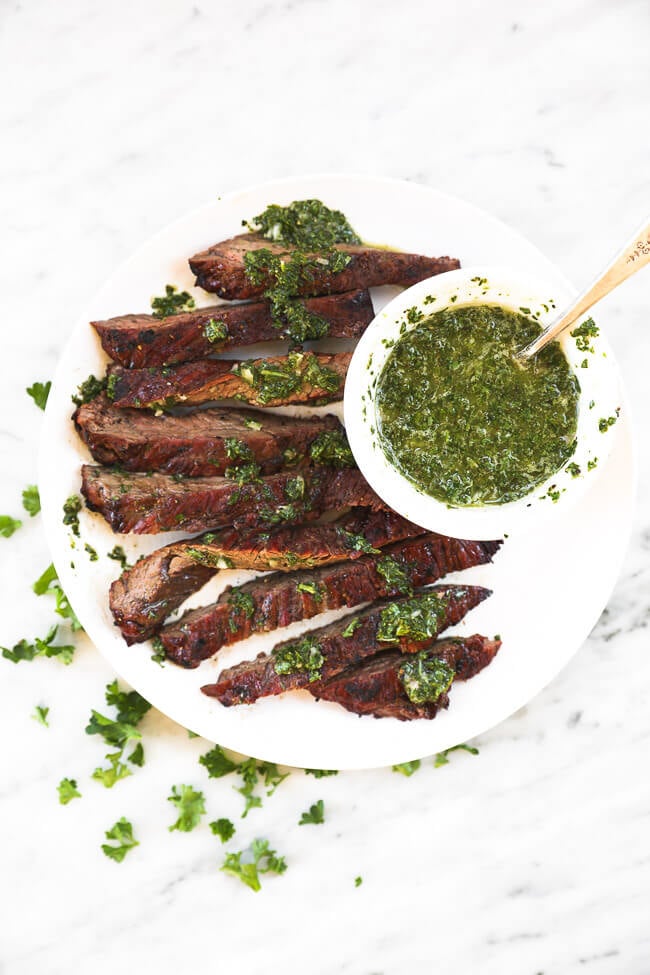 Overhead shot of sliced skirt steak on a white plate with chimichurri sauce over the steak and on the side