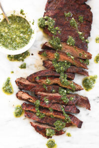 Skirt steak sliced on a marble board with fresh chimichurri sauce drizzled on top