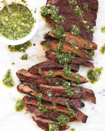 Skirt steak sliced on a marble board with fresh chimichurri sauce drizzled on top