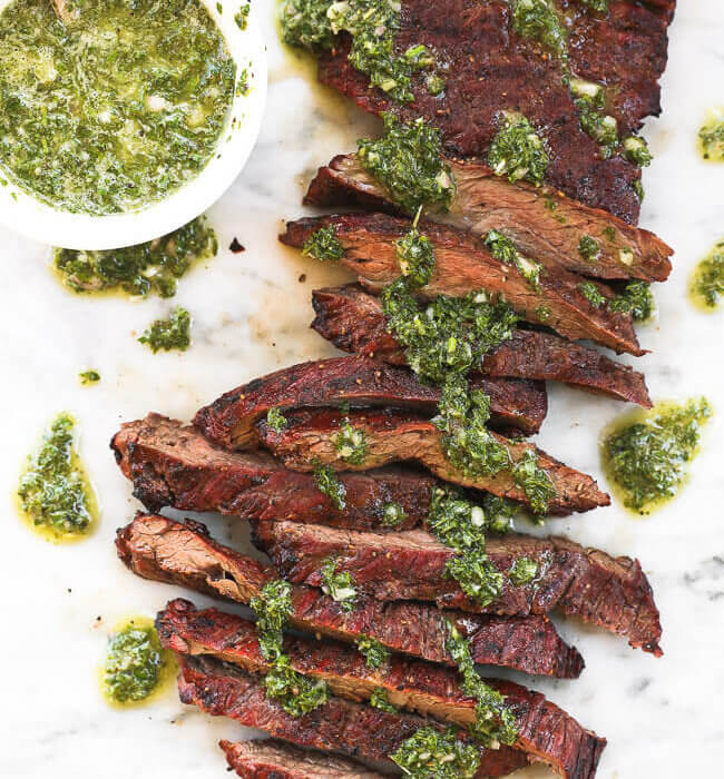 Skirt steak sliced on a marble board with fresh chimichurri sauce drizzled on top