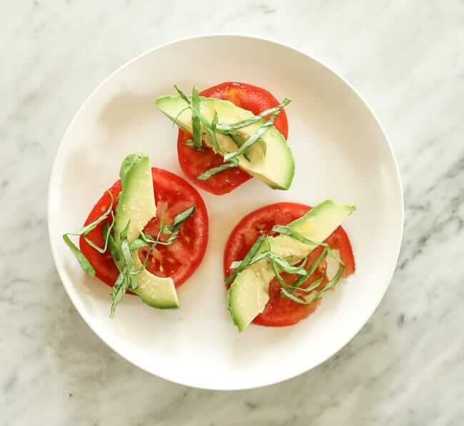 Slices of tomatoes topped with avocado and basil strips on a plate
