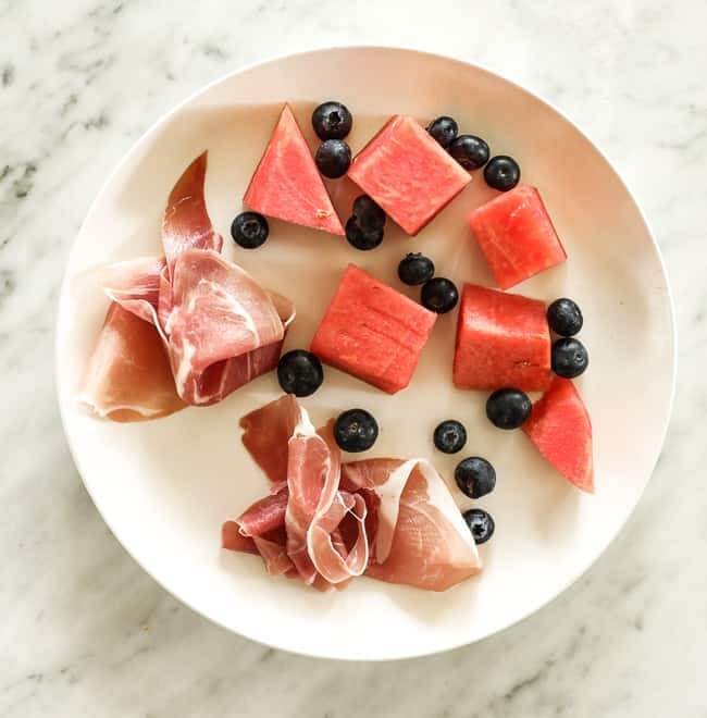 Prosciutto, blueberries and chunks of watermelon on a plate