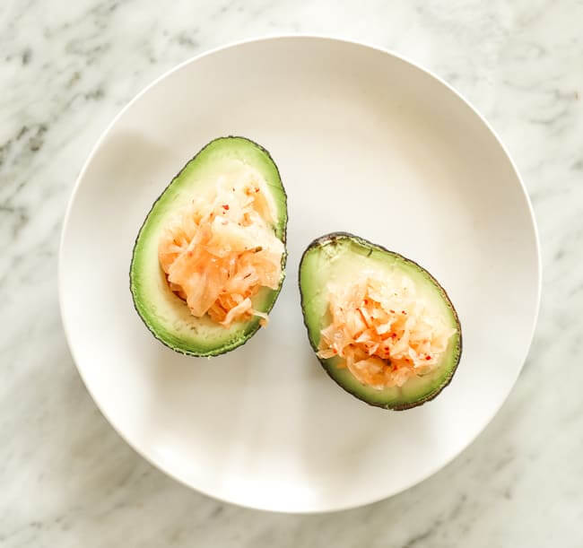 Avocado cut in half and stuffed with kimchi on a plate