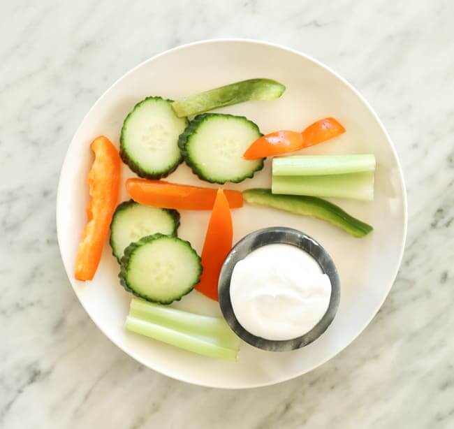 Sliced cucumber, celery and bell pepper on a plate with coconut yogurt