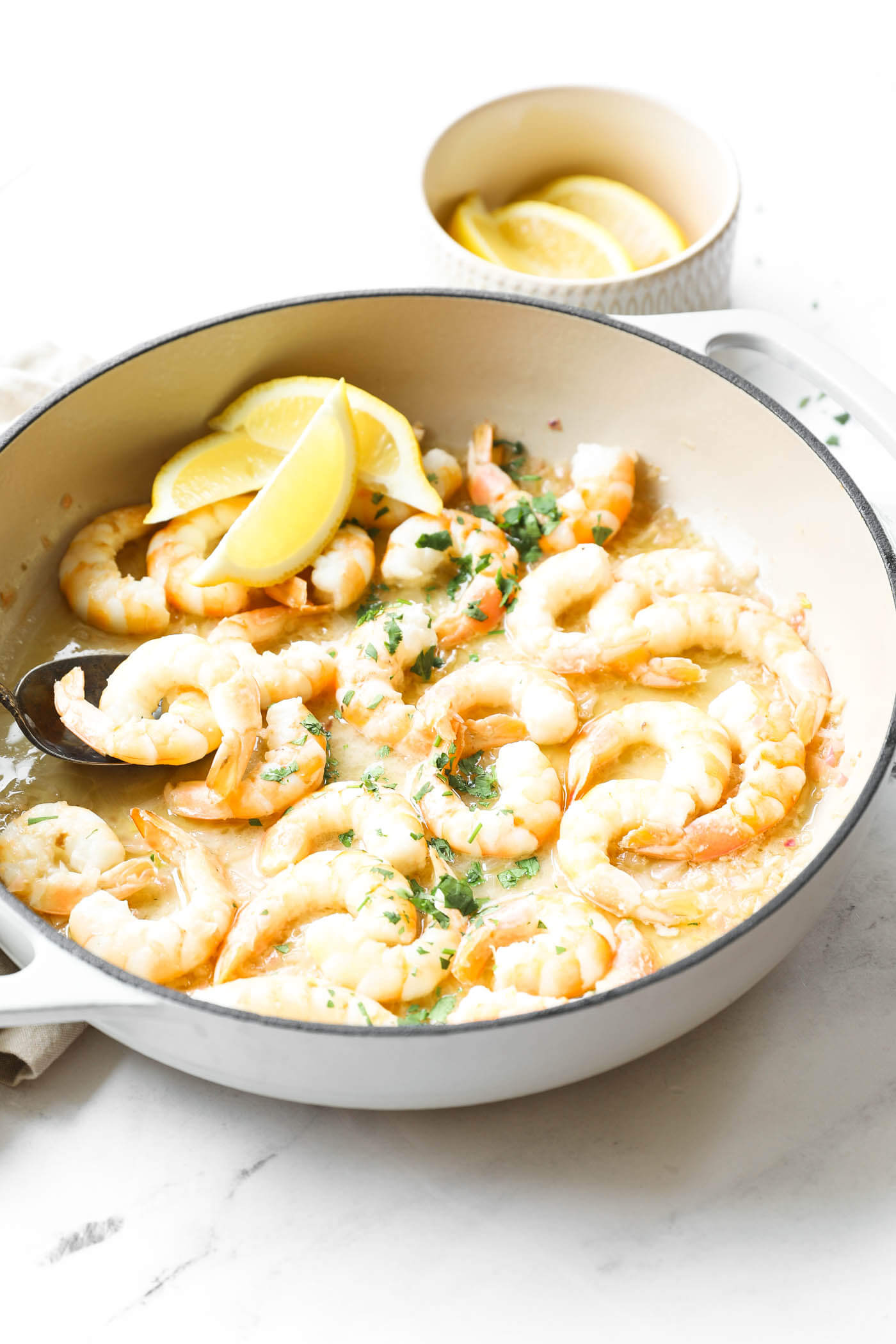 Angled image of garlic butter shrimp in a skillet. Topped with chopped cilantro and lemon wedges.