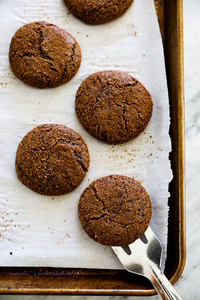 Overhead vertical image of ginger molasses cookies on a sheet pan with spatula lifting one cookie. 