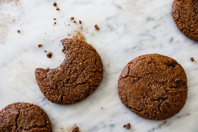 Overhead horizontal image of ginger molasses cookies on marble with a bite taken out of one cookie. 