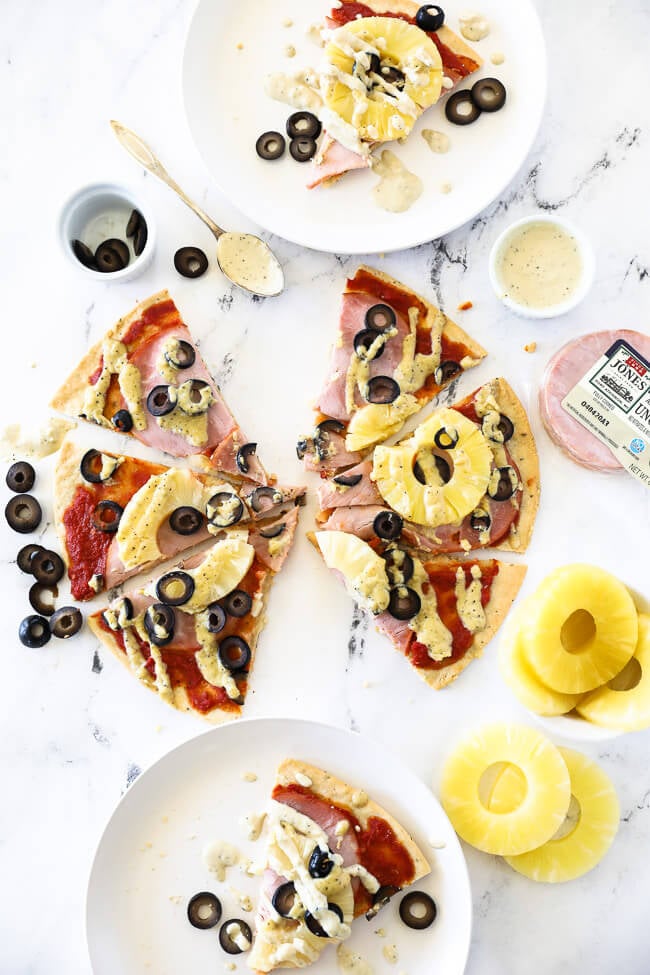 vertical overhead image of hawaiian pizza cut into slices on marble and then served up on two plates with extra dairy free sauce drizzled on top. 