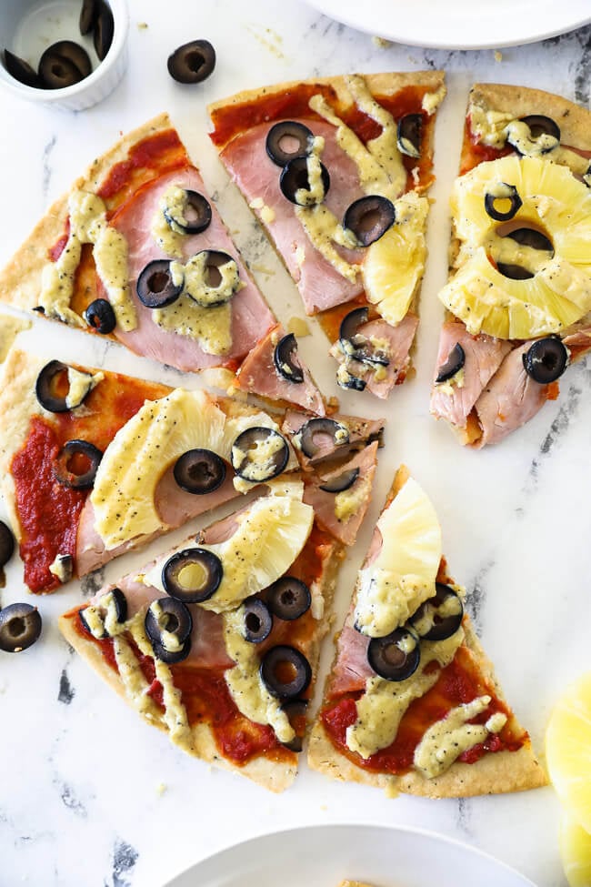 Overhead vertical image of hawaiian pizza sliced into pieces and spread out on marble. 