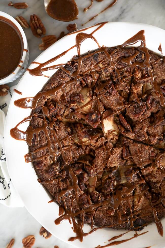 Close up image of gluten-free apple cake in a pie dish with lots of caramel sauce drizzled on top. 