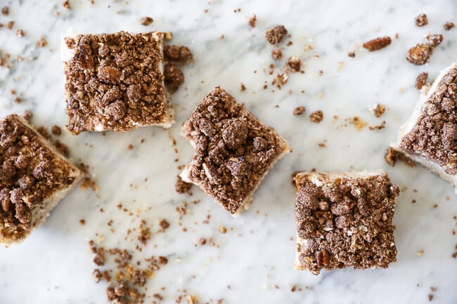 Squares of gluten free coffee cake spread out in a horizontal snake like line on marble with crumbs all over. 